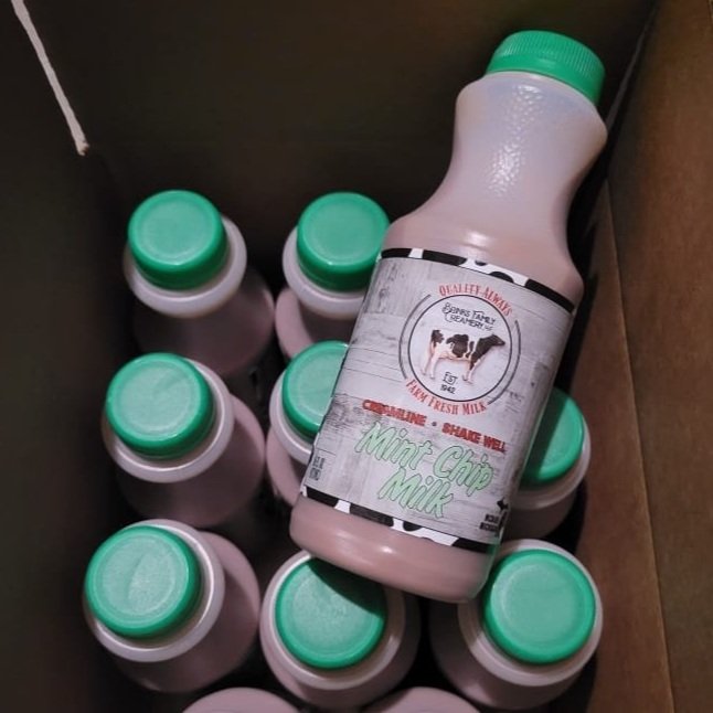 Bottles of mint chip milk with green caps in a cardboard box, showcasing a label that emphasizes fresh quality from a local farm.