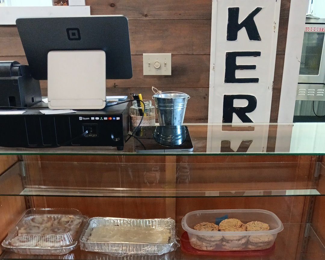 Point of sale system at a bakery with glass display showcasing baked goods, including cinnamon rolls, cookies, and icing. A rustic wooden backdrop enhances the warm atmosphere of the shop.