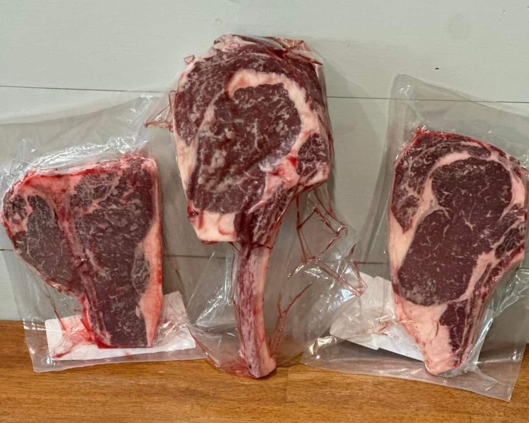 Brinks+Family+Creamery+-+FB_IMG_1730136530294 Three vacuum-sealed cuts of premium beef, including ribeye and tomahawk steaks, displayed on a wooden surface, showcasing their marbled texture and freshness. Ideal for grilling or special occasions.