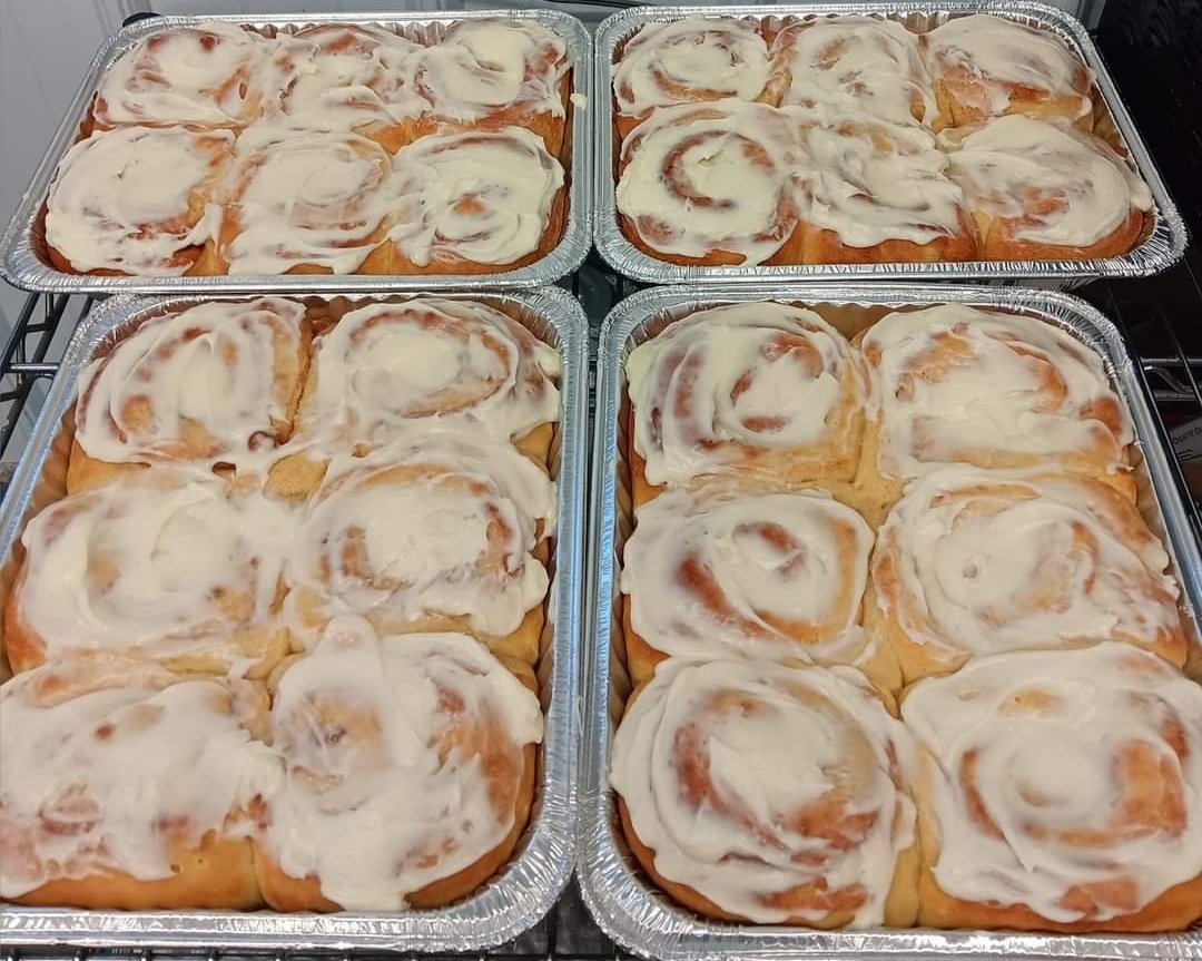 Brinks+Family+Creamery+-+FB_IMG_1730136546297 Freshly baked cinnamon rolls topped with creamy icing, displayed in two aluminum trays. Each tray contains a dozen soft, fluffy rolls, showcasing their swirled cinnamon filling and generous frosting. Perfect for dessert or a sweet breakfast treat.